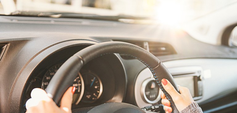 Carro visto por dentro. Mão feminina segura volante com brilho do sol ao lado. Carro visto por dentro. Mão feminina segura volante com brilho do sol ao lado.