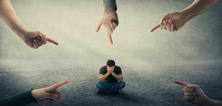 Imagem com cinco mãos apontando para um homem, com as mãos no rosto, sentado ao centro Imagem com cinco mãos apontando para um homem, com as mãos no rosto, sentado ao centro