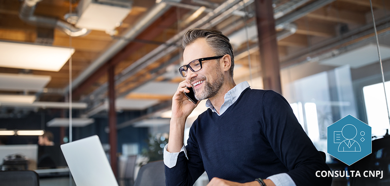 Homem em sua mesa de trabalho utilizando o celular e o computador Homem em sua mesa de trabalho utilizando o celular e o computador