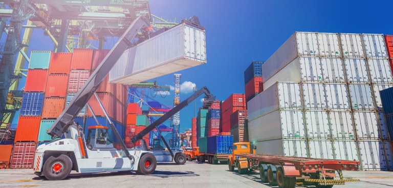 Foto de um pátio cheio de containers de variadas cores, um veículo com guindaste movimenta um container. Foto de um pátio cheio de containers de variadas cores, um veículo com guindaste movimenta um container.