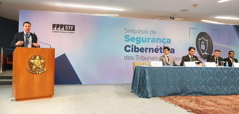 Tiago Iahn palestra no púlpito em Simpósio de Segurança Cibernética dos tribunais superiores, ao seu lado, quatro participantes assistem sentado à mesa.jpg Tiago Iahn palestra no púlpito em Simpósio de Segurança Cibernética dos tribunais superiores, ao seu lado, quatro participantes assistem sentado à mesa.jpg
