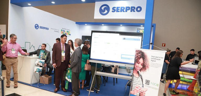 Imagem apresenta o estande o Serpro com pessoas conversando. Crédito: CNM Imagem apresenta o estande o Serpro com pessoas conversando. Crédito: CNM