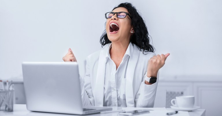 Mulher de cabelos cacheados comemora em frente ao notebook.jpg