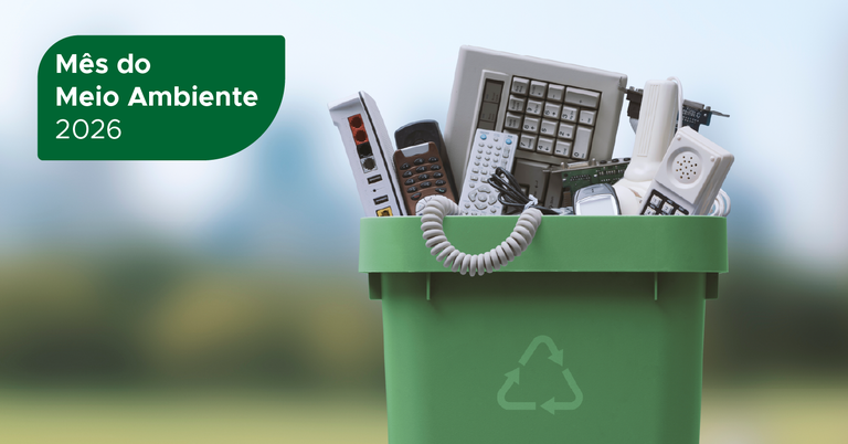 Caixa verde de reciclagem para lixo eletrônico contendo telefones, teclado, roteador e outros equipamentos eletrônicos descartados, com o texto “Mês do Meio Ambiente 2026”. Caixa verde de reciclagem para lixo eletrônico contendo telefones, teclado, roteador e outros equipamentos eletrônicos descartados, com o texto “Mês do Meio Ambiente 2026”.