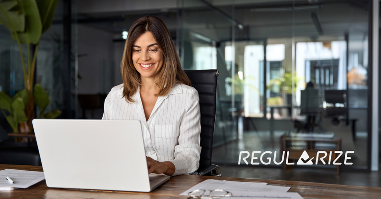 Mulher sorridente trabalha em um notebook em escritório. No lado direito da imagem está aplicada a marca do Portal Regularize Mulher sorridente trabalha em um notebook em escritório. No lado direito da imagem está aplicada a marca do Portal Regularize
